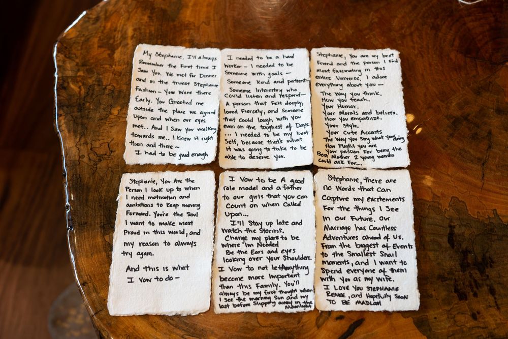 Handwritten wedding vows arranged on rustic wood surface, featuring heartfelt personal messages on aged paper cards.