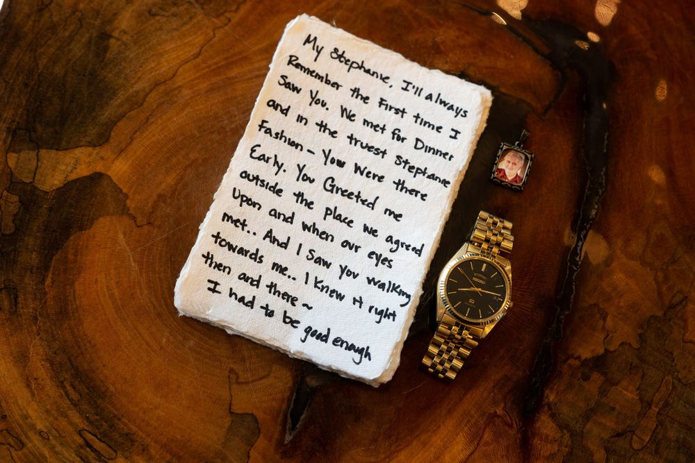 Handwritten love letter on white fabric beside a gold watch on a wooden surface, wedding keepsake gift.