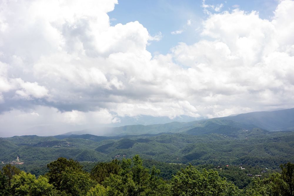 Panoramic view of lush green Smoky Mountains under dramatic white clouds and blue sky.