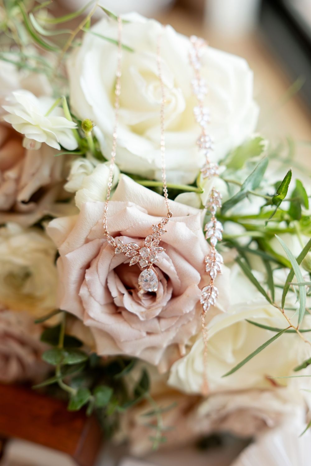 Elegant rose gold diamond necklace draped over blush and white roses in a bridal bouquet with greenery.