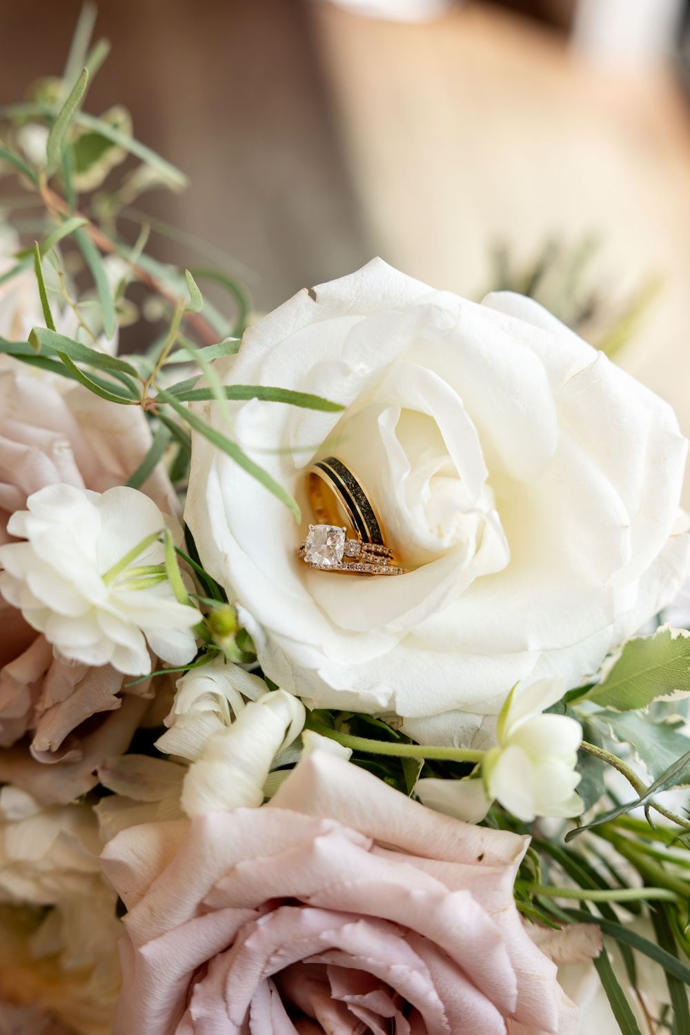Wedding rings nestled in a white rose bouquet with blush pink roses and greenery.