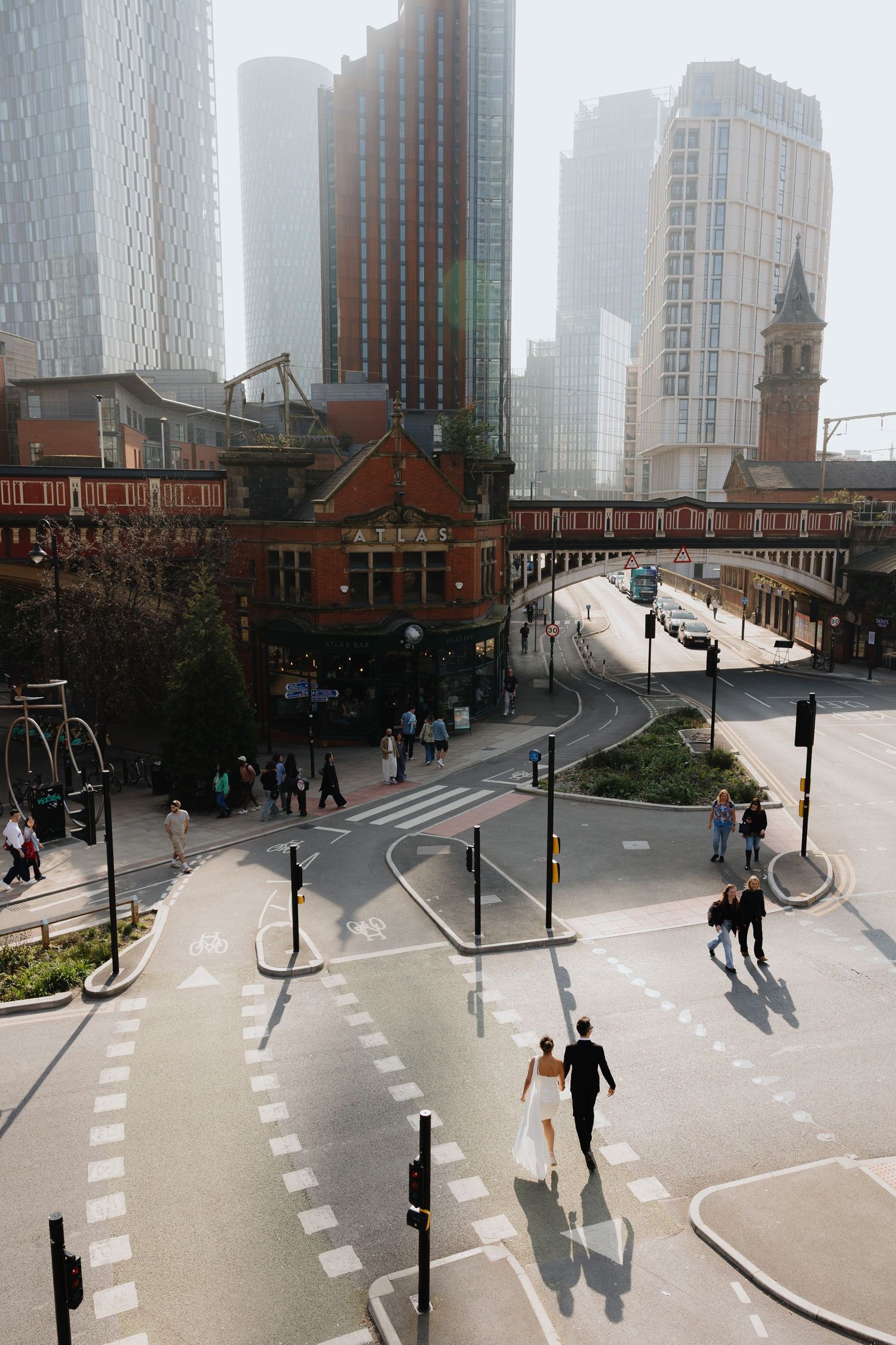 Bride and groom cross a busy urban intersection surrounded by modern skyscrapers and historic buildings in a vibrant city.