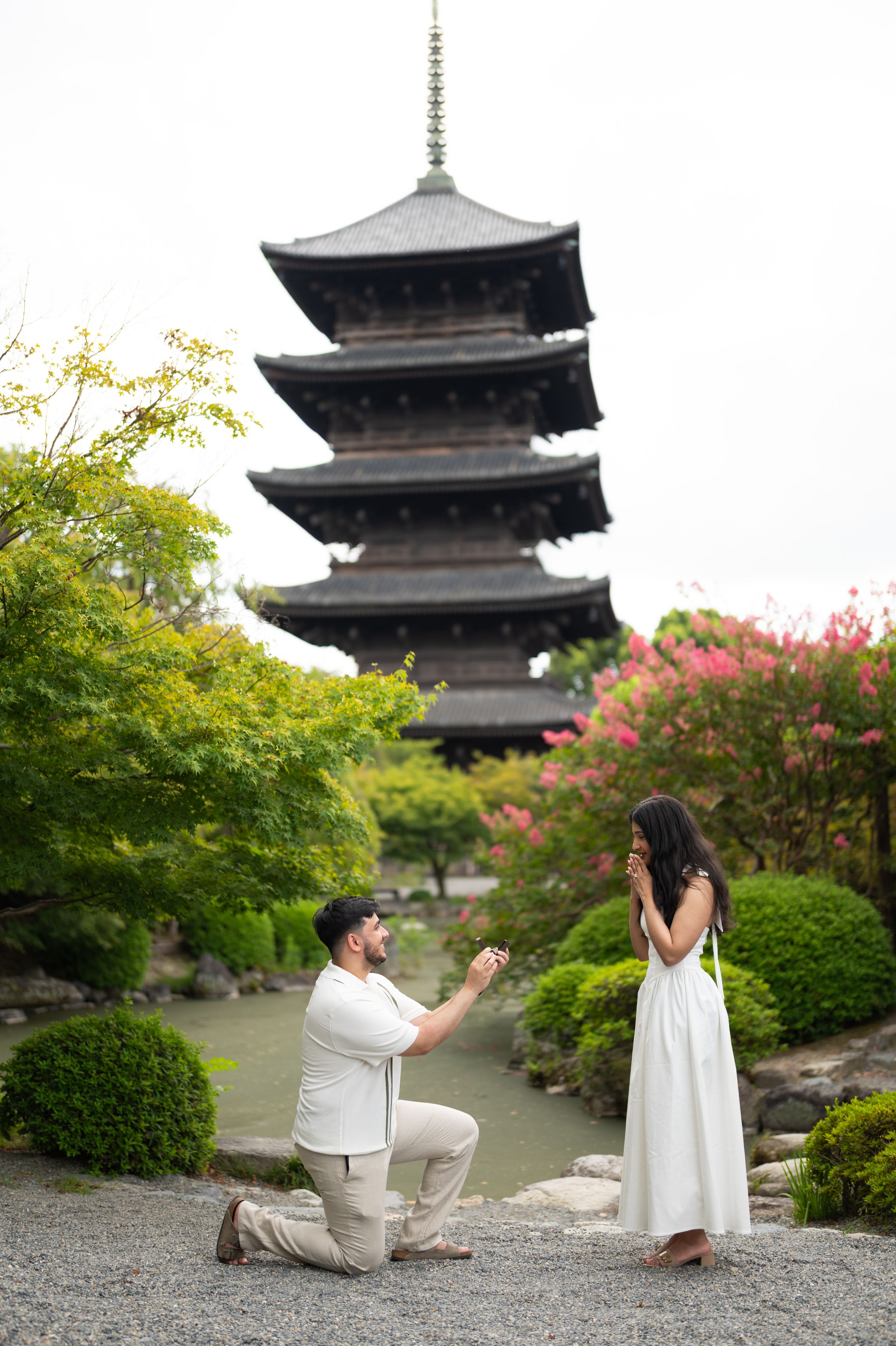 Couple standing on a wooden bridge surrounded by lush green trees in a Japanese garden.