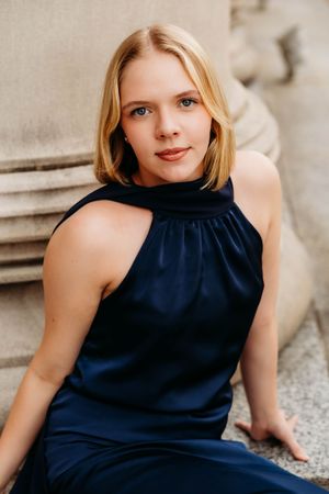 Young blonde woman in navy halter dress poses gracefully on stone steps in an elegant outdoor portrait.