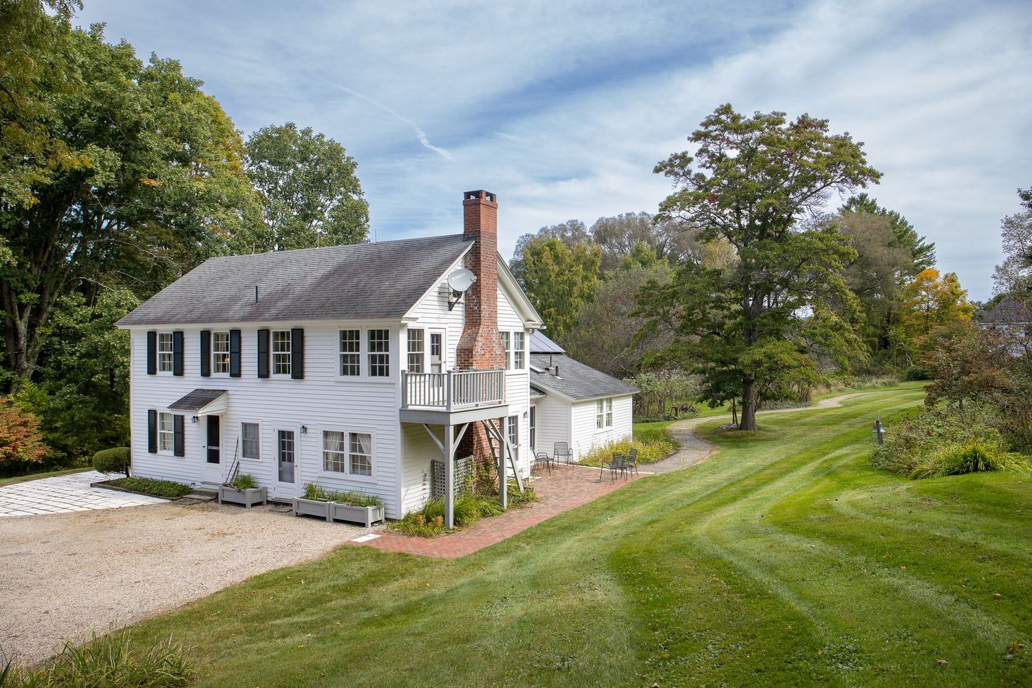 Classic white colonial farmhouse with black shutters set on a rolling green landscape.