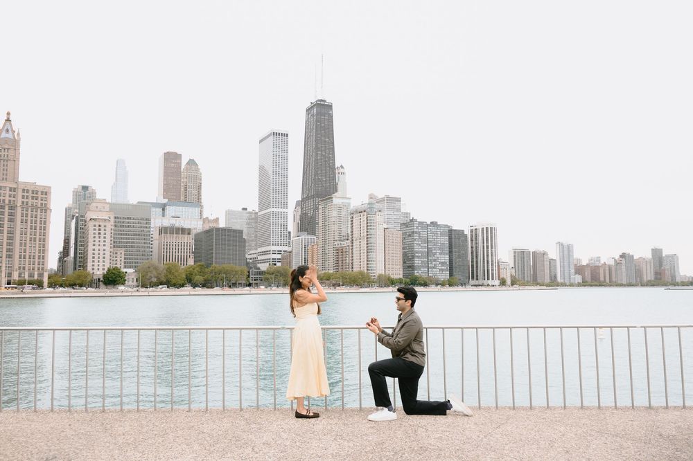 Man proposes to woman on one knee by Chicago skyline waterfront on a clear day.