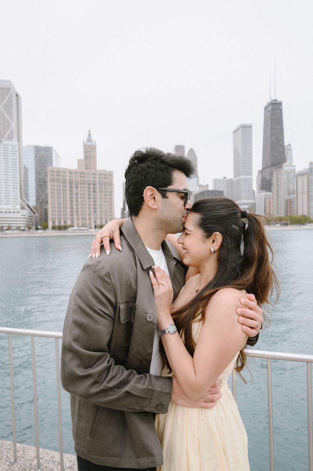 Couple sharing a romantic kiss on a waterfront with Chicago skyline and John Hancock Tower in the background.