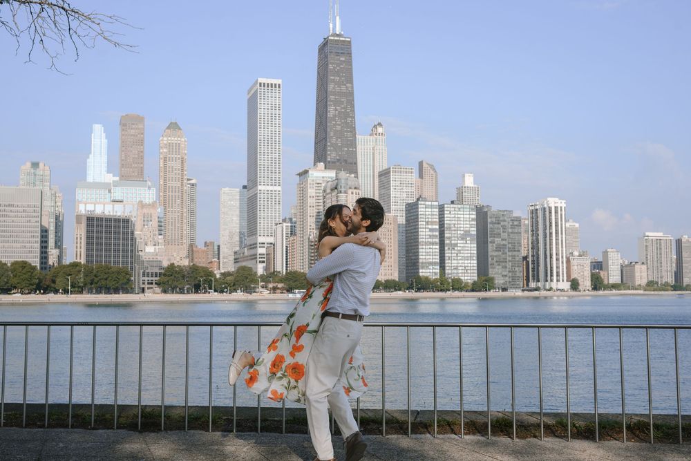 Couple embracing and kissing in front of the Chicago skyline with the John Hancock Center visible behind them.