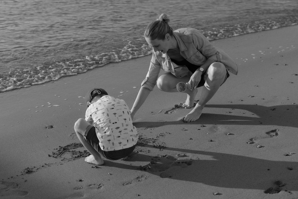 Woman and child playing in wet sand at the beach shoreline in black and white photo.