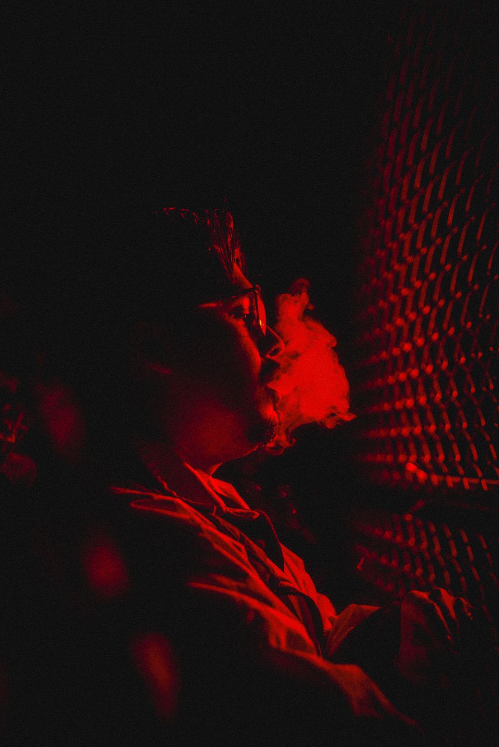 Person exhaling smoke under dramatic red lighting in a dark atmospheric setting.