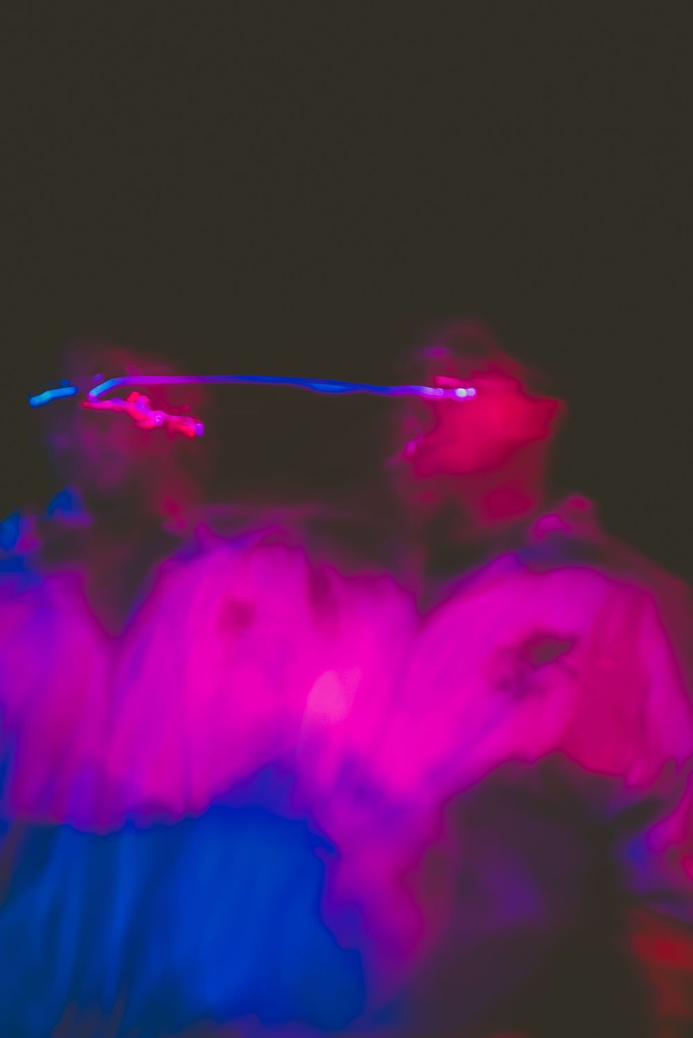 Vibrant pink and blue smoke swirls in darkness with glowing neon light streaks creating an abstract artistic composition.