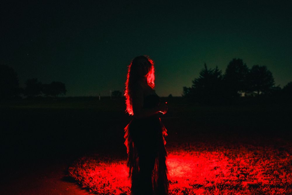 A silhouette of a person illuminated by red light stands in an open field at night.