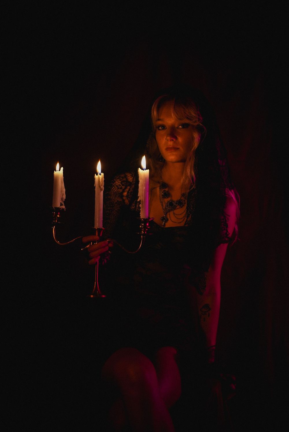 Woman in black lace holding candelabra with lit candles in dramatic dark setting.