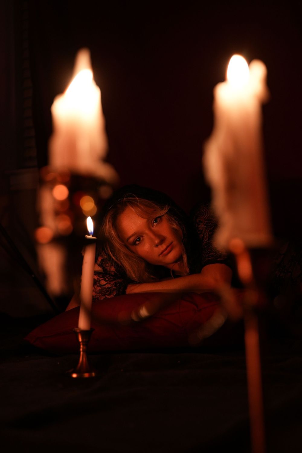 Woman gazing through candlelight in a dark romantic setting with glowing candles in the foreground.