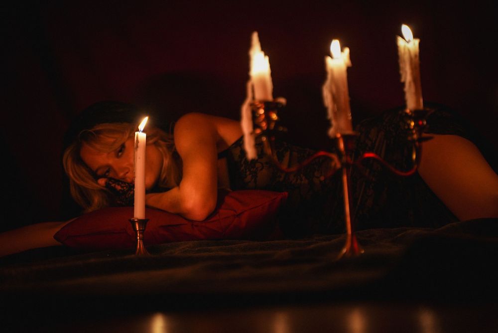 Woman lying near a candelabra with lit candles in a dimly lit romantic setting.