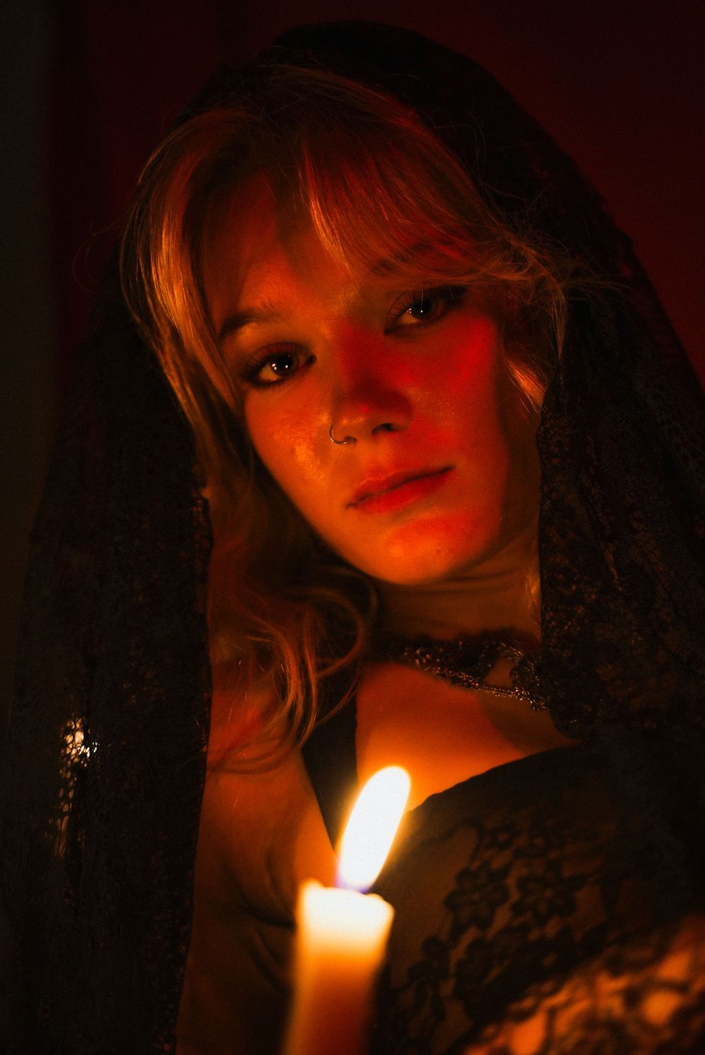 Young woman in black lace veil holding glowing candle in dramatic candlelight portrait.