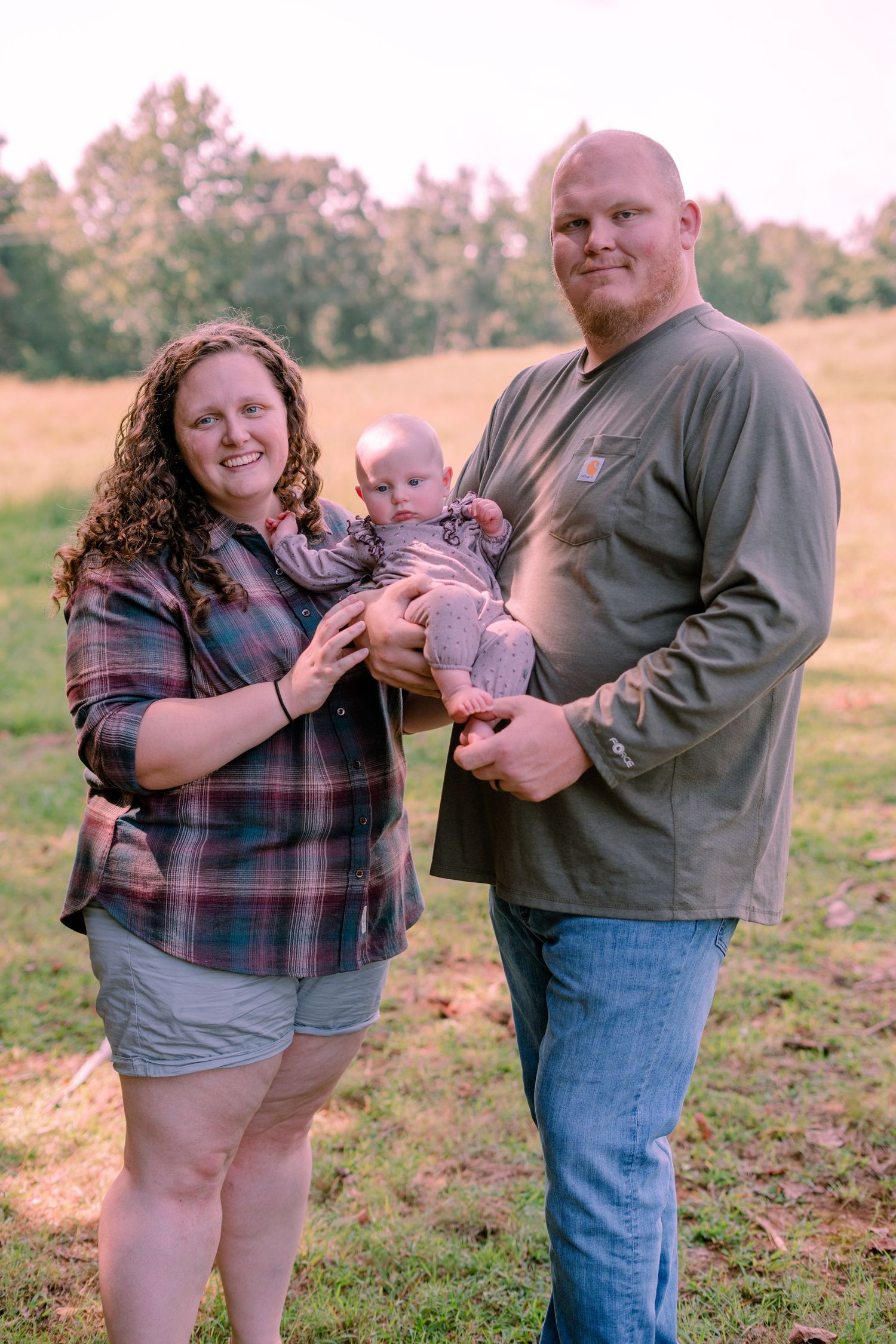 Smiling young family holding their baby in a golden hour outdoor field setting.
