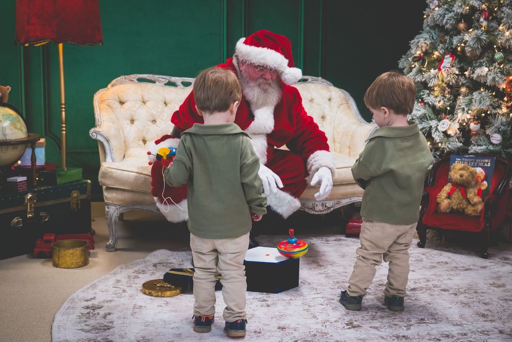 Two toddlers meet Santa Claus in a festive Christmas decorated room with a tree and elegant cream sofa.