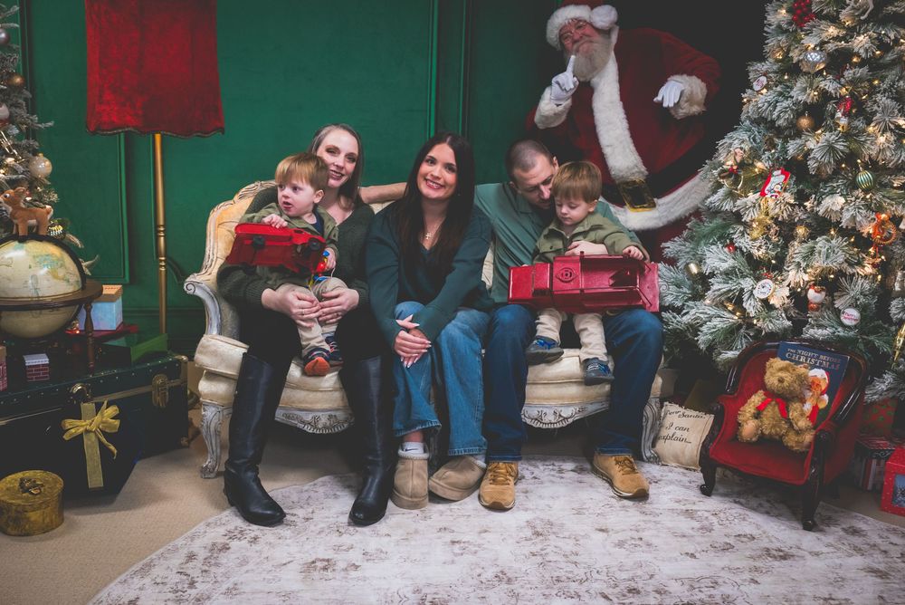 A family of four poses with Santa Claus beside a decorated Christmas tree in a festive holiday setting.
