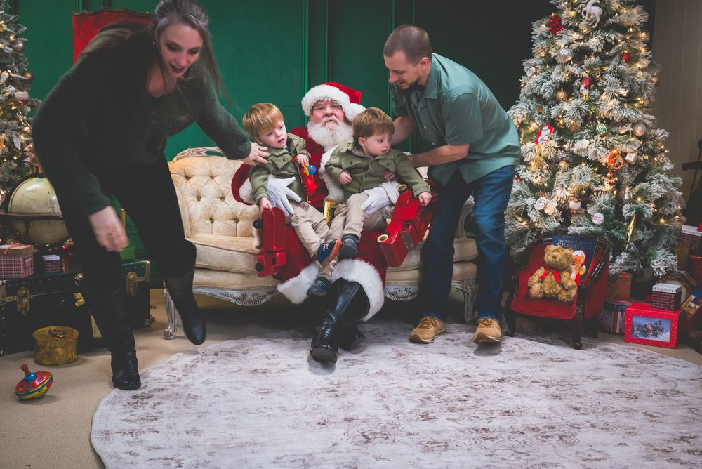 Family with two young children taking a holiday photo with Santa Claus beside a decorated Christmas tree.