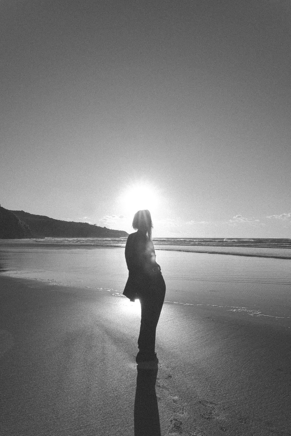 Black and white photo of a woman silhouetted against the sun on a beach.