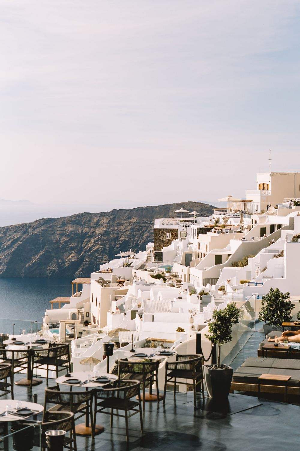 Scenic Santorini cliffside restaurant terrace with white-washed buildings cascading down to the Aegean Sea, Greece.