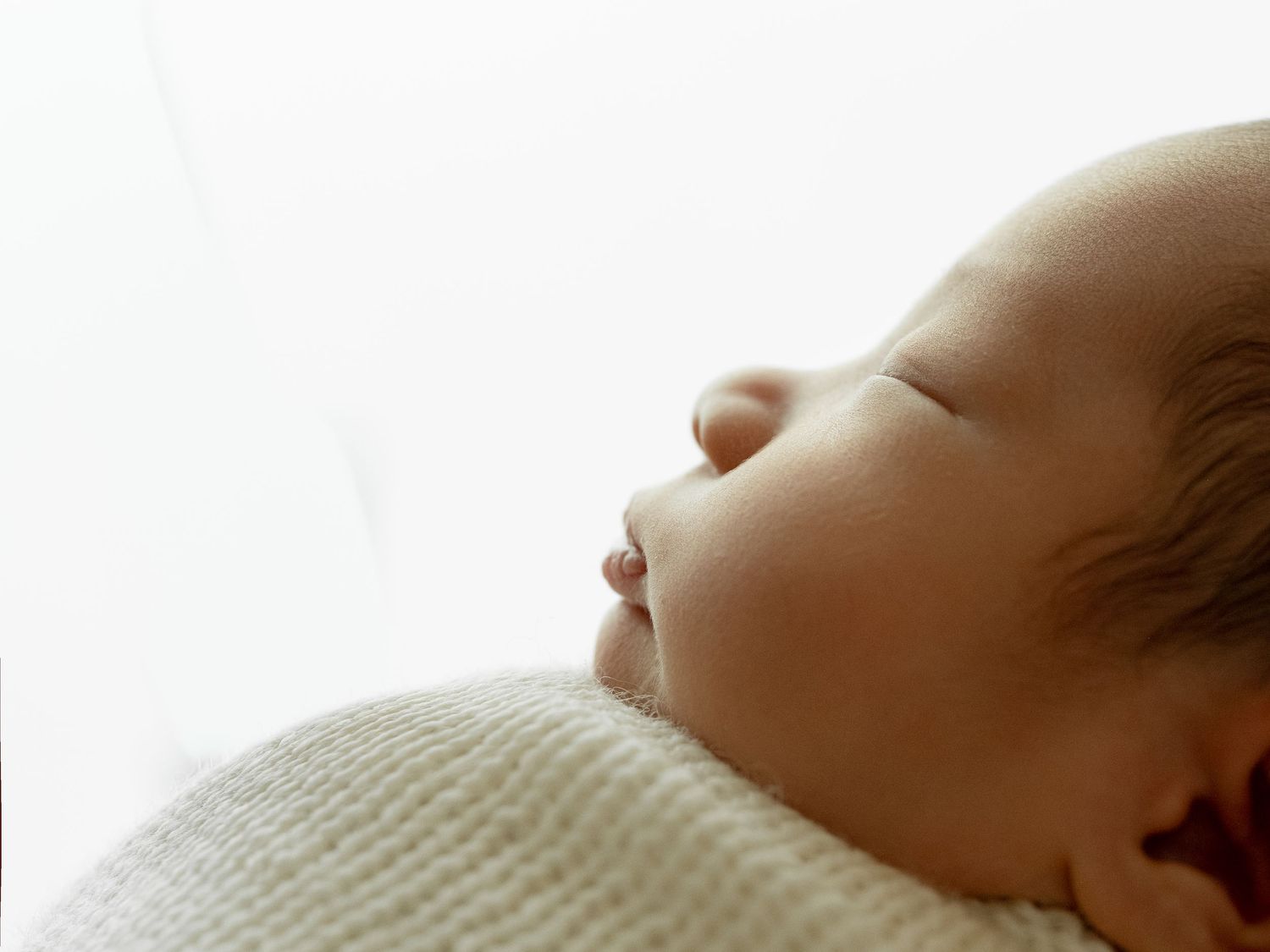 Peaceful newborn baby sleeping wrapped in soft white blanket, close-up portrait on white background.
