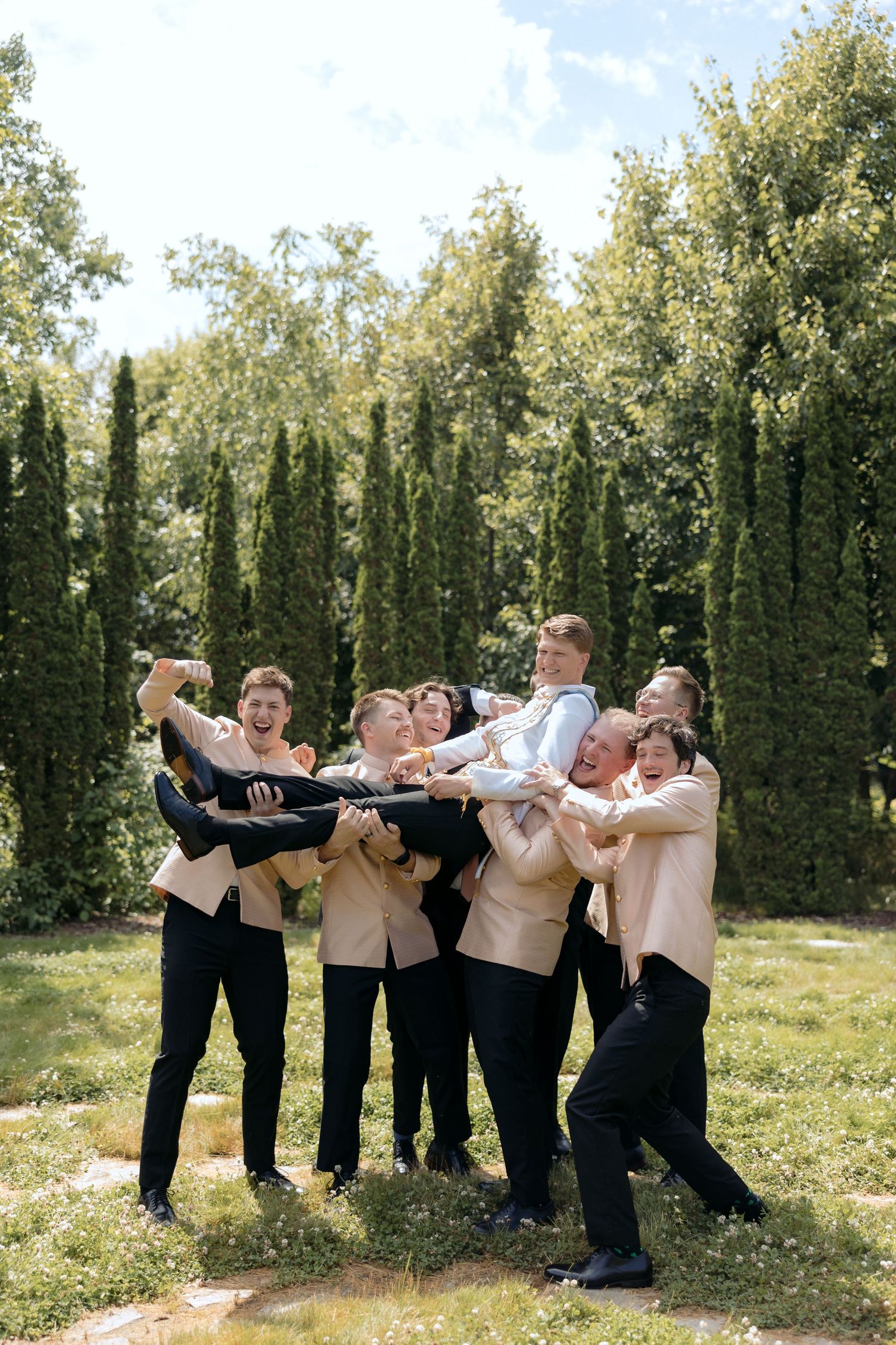 Groomsmen in traditional Cambodian attire lift their groom into the air to celebrate his wedding day at this Twin Cities MN Wedding.