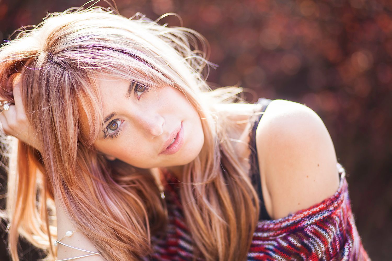 Young woman with highlighted blonde hair posing outdoors with bokeh autumn background.