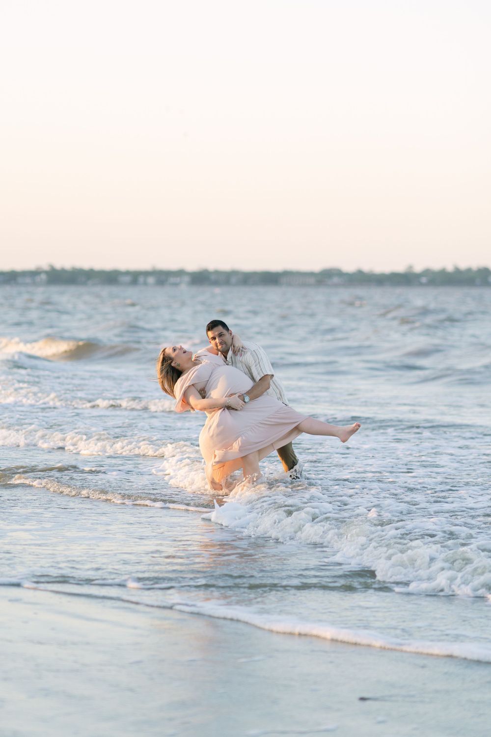 Expectant parents laughing and playing in the shallow surf at sunset on Jekyll Island.