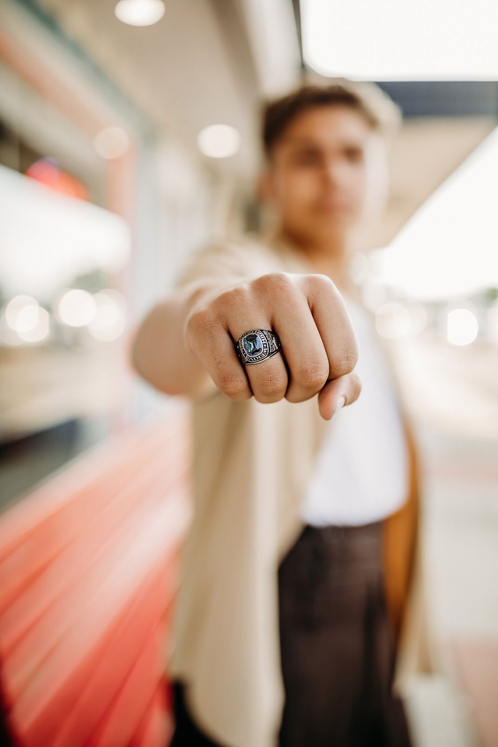Young man in beige jacket showing off a silver championship ring on his fist toward the camera.