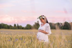 Gravid kvinna står och tittar ner på sin mage och drömmer om framtiden i ett rågfält med blåklint. Bakom henne skiftar himlen i rosa och li