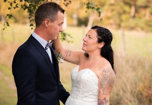 A tattooed bride gazes lovingly at her groom while standing together in an autumn outdoor setting.
