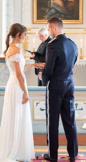 Bride and groom exchanging rings at church altar during wedding ceremony with officiant in background.