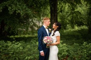 Bride and groom gazing at each other in lush green garden setting with pink bridal bouquet.
