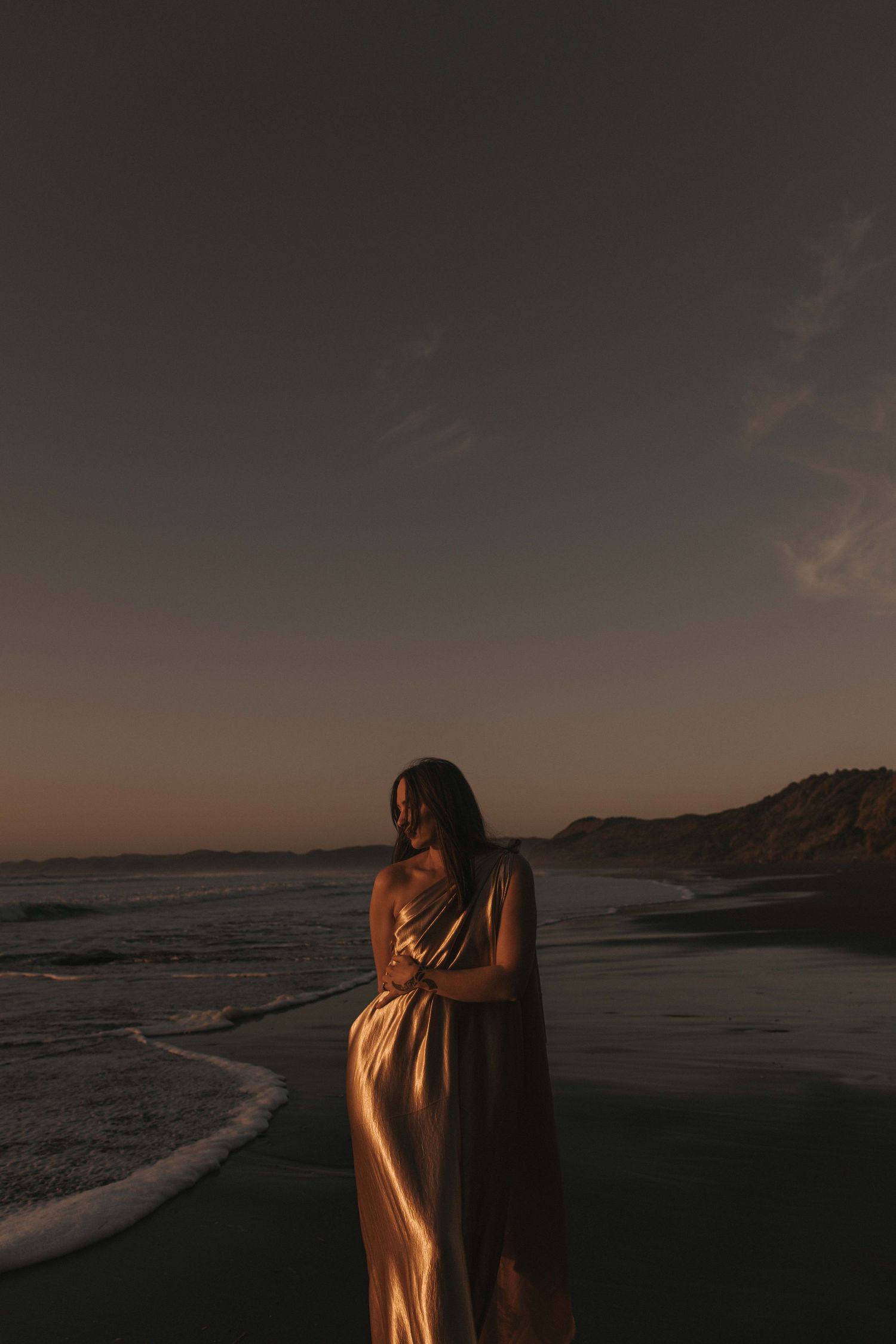 Woman draped in gold fabric on Raglan's black sand beach at sunset — Goddess Shoot® by Nami Creative
