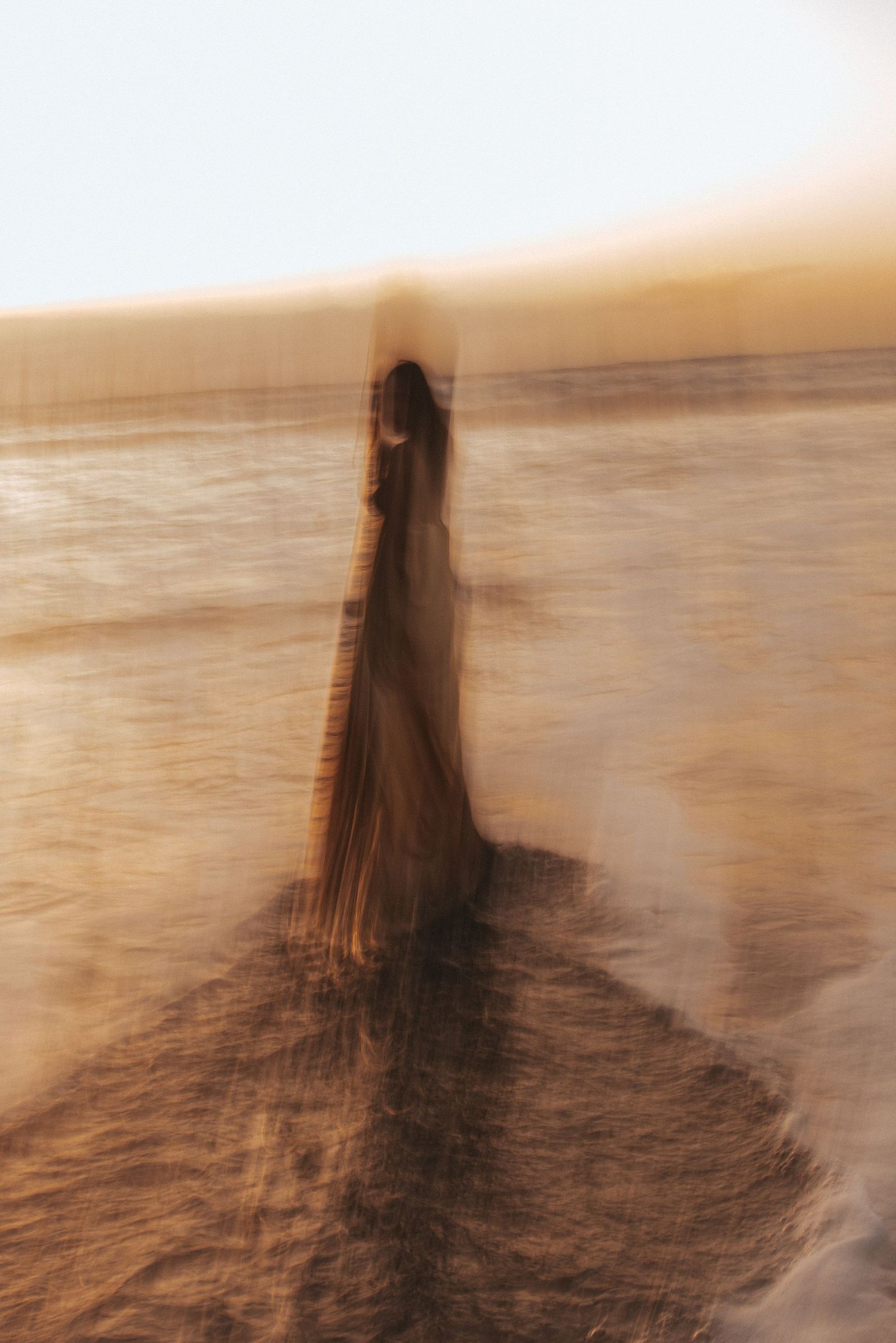 Blurred motion photo of a woman in a flowing dress standing on a beach at golden sunset.
