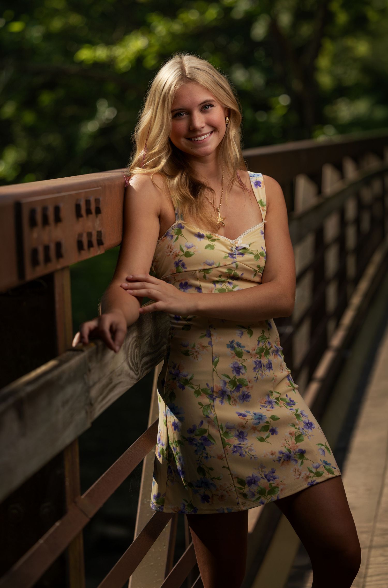 Senior portrait of a blonde girl in a floral dress on a wooden bridge