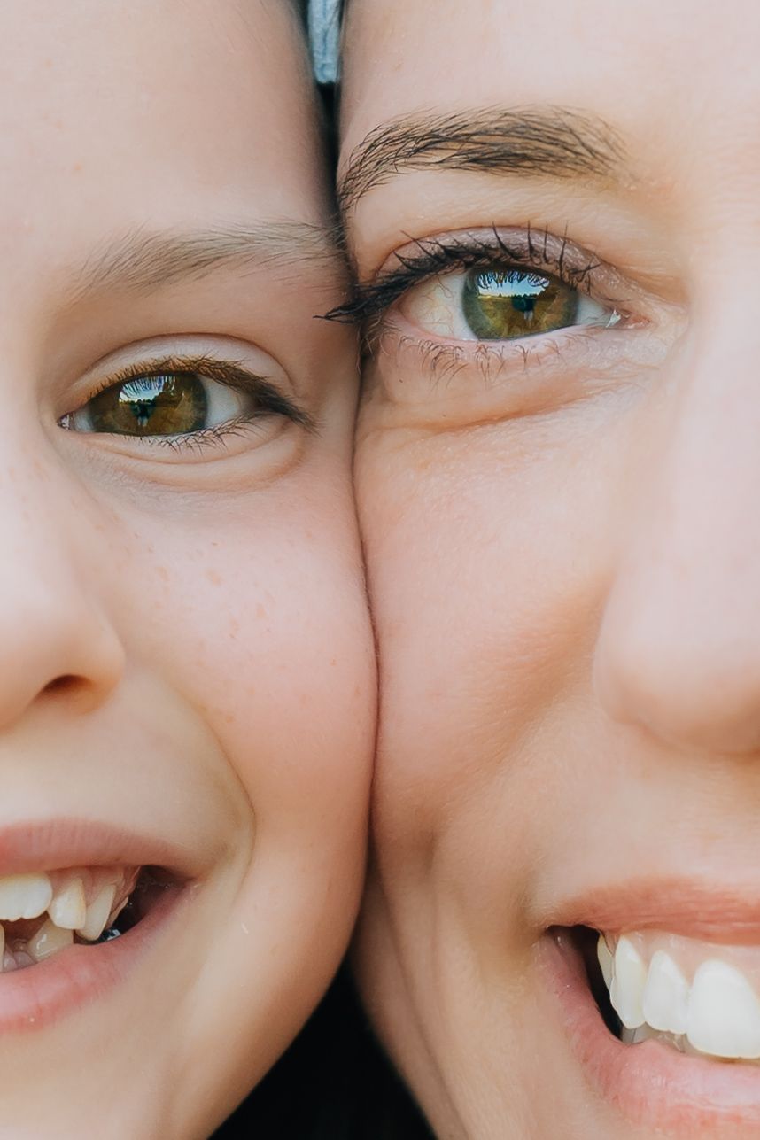 Close-up portrait of two children with green eyes and bright smiles pressed cheek to cheek.
