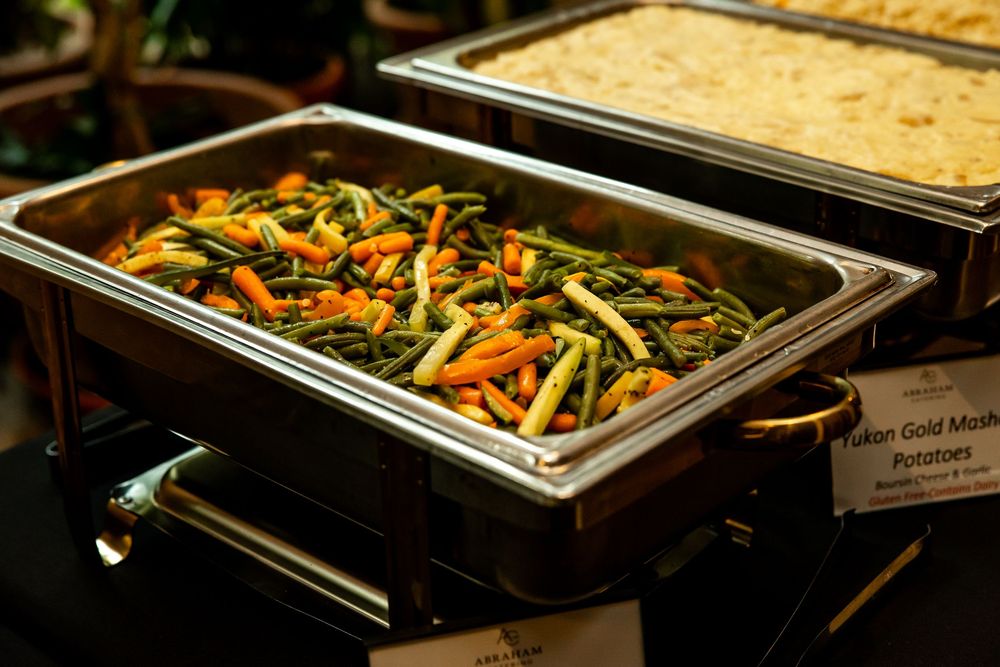 Buffet chafing dish filled with fresh green beans and carrots alongside Yukon Gold mashed potatoes at a catered event.