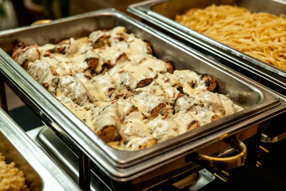Buffet chafing dishes with creamy mushroom chicken and pasta at a catered event.