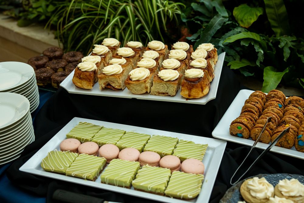 Elegant dessert buffet table with petit fours, macarons, cinnamon rolls, and pastries arranged on white platters.
