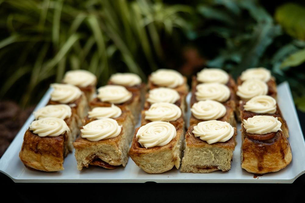 A tray of mini cinnamon rolls topped with swirled cream cheese frosting displayed on a white platter.