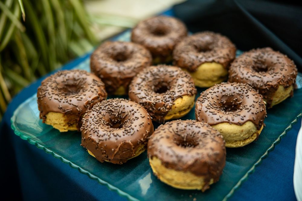 Chocolate glazed donuts with sesame seeds arranged on a teal tray at an outdoor event.