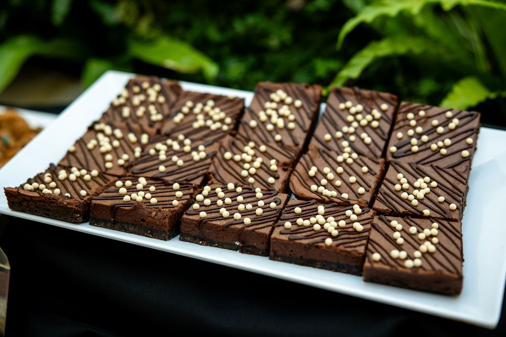 Chocolate brownie bars topped with white chocolate pearls and drizzle on a white platter outdoors.