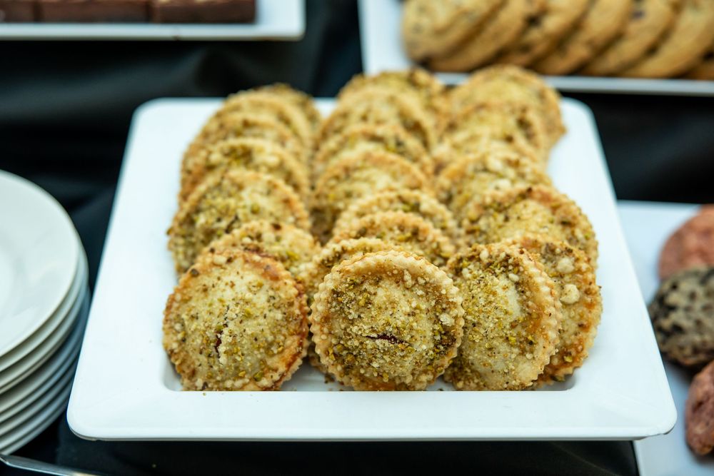 A white rectangular platter filled with rows of sesame-coated round pastries or cookies at a catering event.