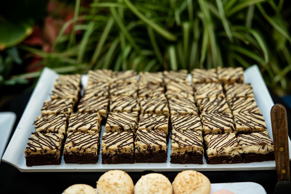 Tray of chocolate brownies with caramel drizzle cut into squares, displayed beside round truffles at a dessert table.