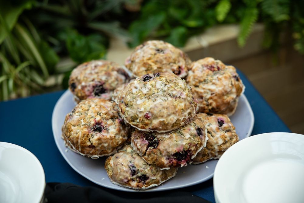 A plate of freshly baked blueberry muffins topped with sugar crystals, served outdoors on a blue table.
