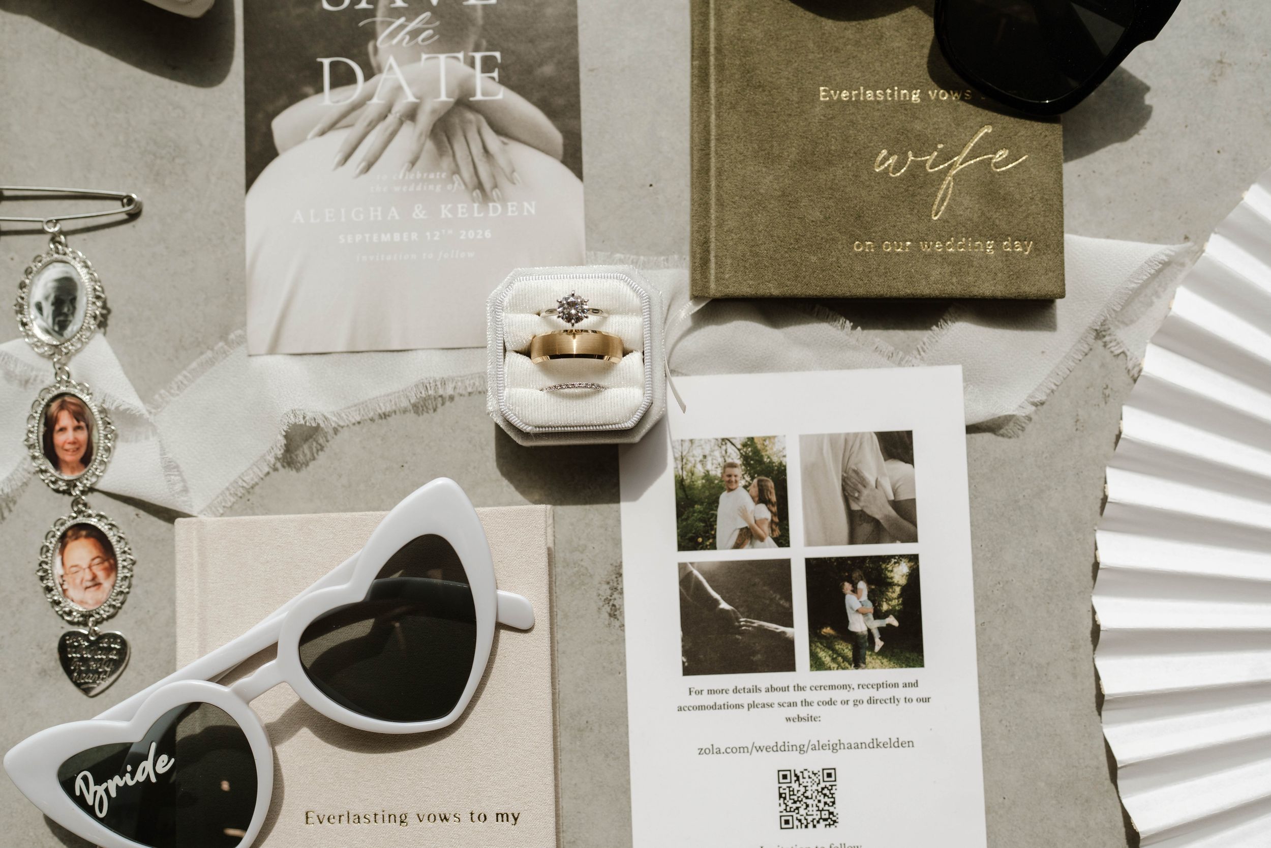 Bridal flat lay featuring heart sunglasses, engagement ring, save the date card, wife book, and wedding stationery on marble.