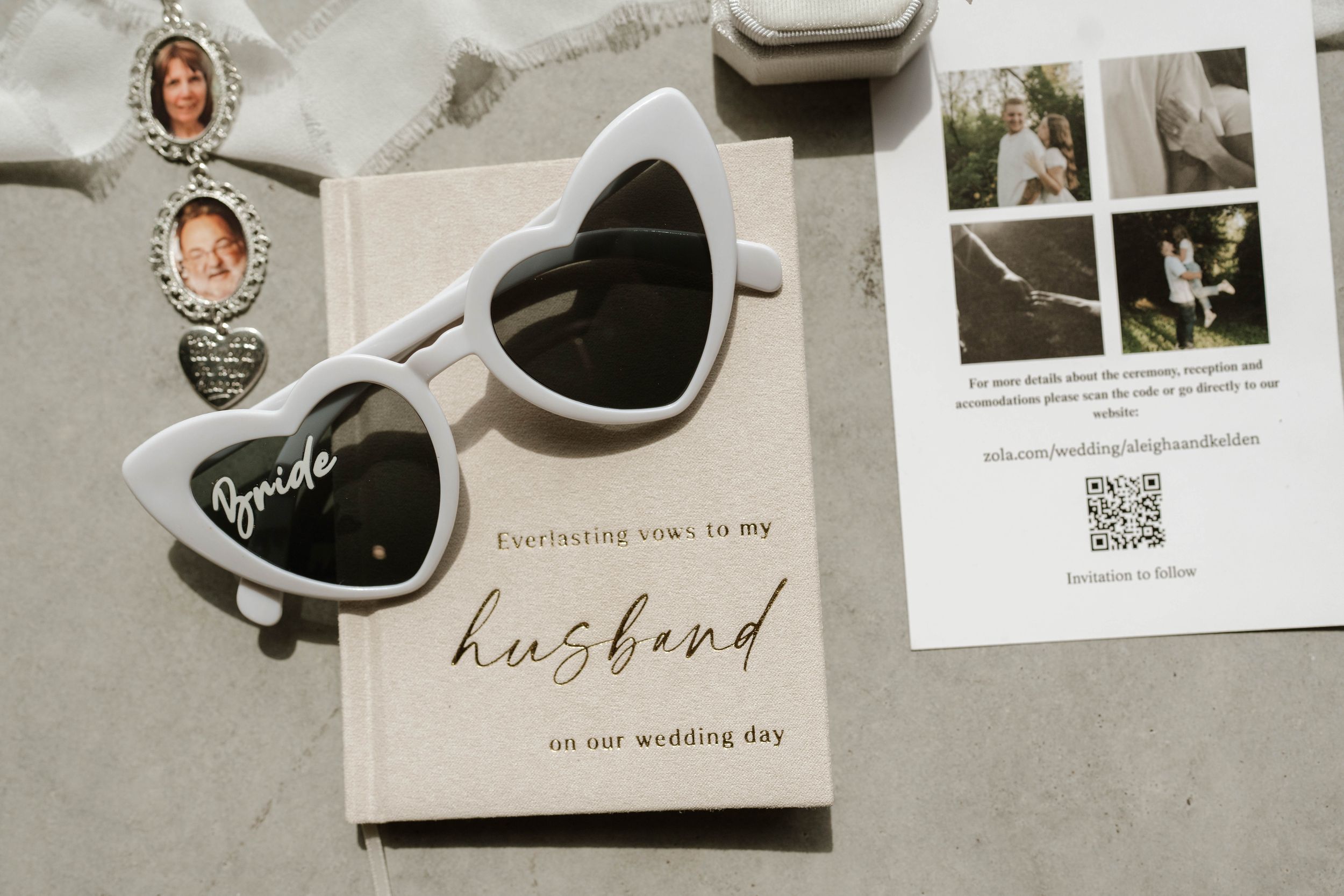 White heart-shaped bride sunglasses resting on a wedding vow book with gold script lettering and bridal accessories.